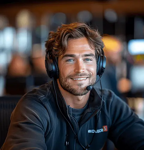 Un homme souriant portant un casque avec micro, travaillant dans un environnement de bureau